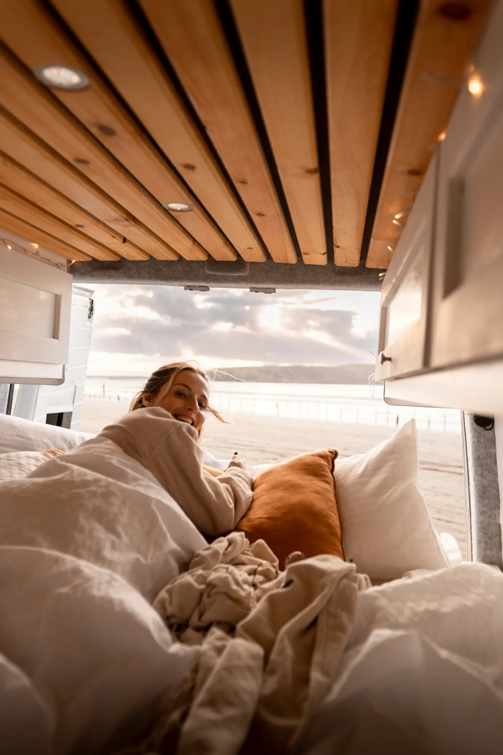 Frau liegt im Wohnmobil mit Blick aufs Meer – gemütliches Reisen mit Roadfun Campern.